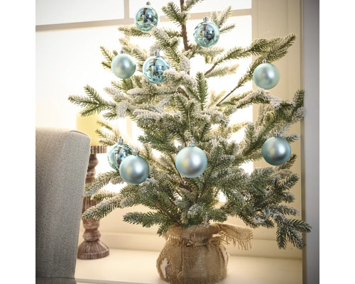 Decoratieve kleine kerstboom met kerstballen in juten zak op vensterbank