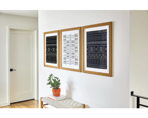 Drie ingelijste afbeeldingen met abstracte patronen hangen aan de muur boven een bank met een plant in een pot.