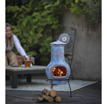 Decoratieve tuinhaard van klei met houtblokken en tuinmeubilair op de achtergrond.