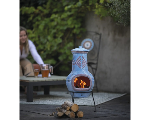 Decoratieve tuinhaard van klei met houtblokken en tuinmeubilair op de achtergrond.