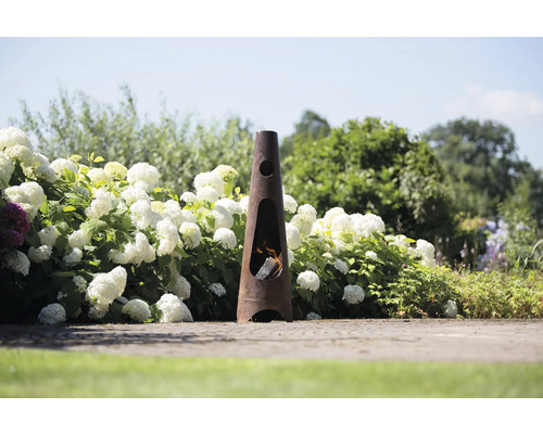Tuinscene met een slanke, kegelvormige metalen open haard, die met hout wordt gestookt en is omgeven door hortensia''s.