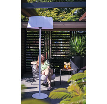 Vrouw zit in de tuin onder een pergola met een staande lamp.
