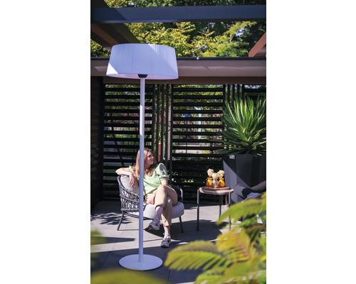Vrouw zit in de tuin onder een pergola met een staande lamp.