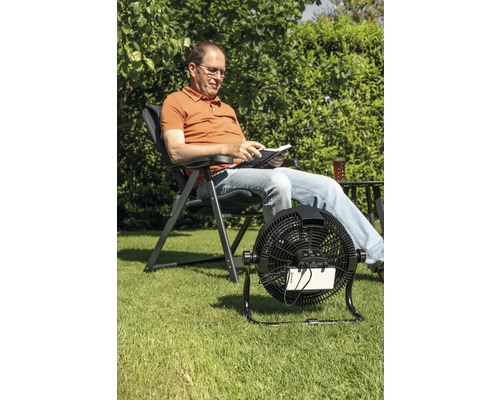 Man leest in de tuin met een draadloze ventilator voor verkoeling