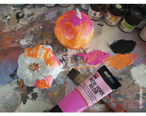 Beschilderde pompoenen met verf, penseel en verftubes op een werkblad.