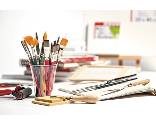 Diverse penselen in een beker, schildersmessen, een verfroller en andere schildersbenodigdheden op een tafel.