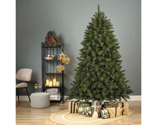 Versierde kerstboom met cadeaus op een gevlochten tapijt in een woonkamer.