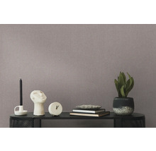 Close-up van een behang met motief met een tafel met een kaars, beeldhouwwerk, klok, boeken en een potplant.