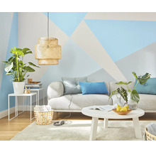 Woonkamer met bank, tafel, lamp en kamerplanten voor een wand met geometrische patronen
