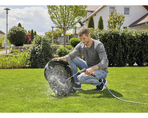 Een persoon reinigt een robotgrasmaaier met een tuinslang op een gazon