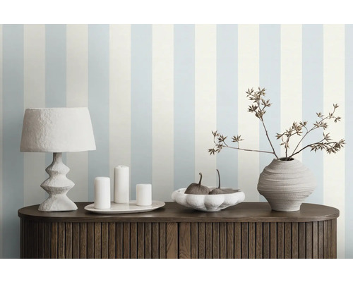 Decoratieve kamer met gestreept behang, tafellamp, kaarsen, schaal en vaas op een kast