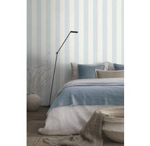 Slaapkamer met bed, staande lamp en gestreept behang voor een lichte sfeer.