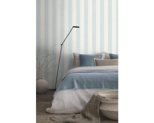 Slaapkamer met bed, staande lamp en gestreept behang voor een lichte sfeer.