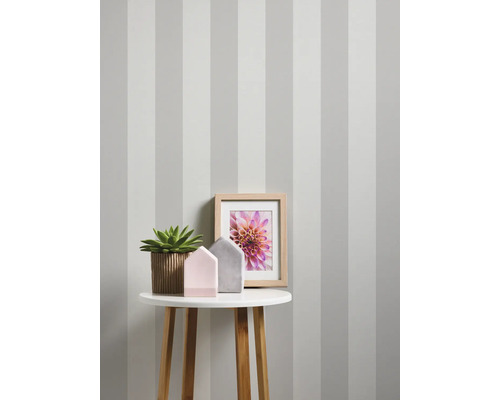 Decoratief interieur met gestreept behang, tafel, plant, fotolijst en decoratie.