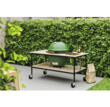 Groene barbecue op een tafel met wielen, zak houtskool in de tuin.