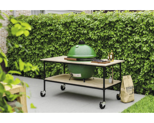 Groene barbecue op een tafel met wielen, zak houtskool in de tuin.