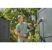 Man reinigt hek met elektrische borstel in de tuin.