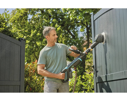 Man reinigt hek met elektrische borstel in de tuin.