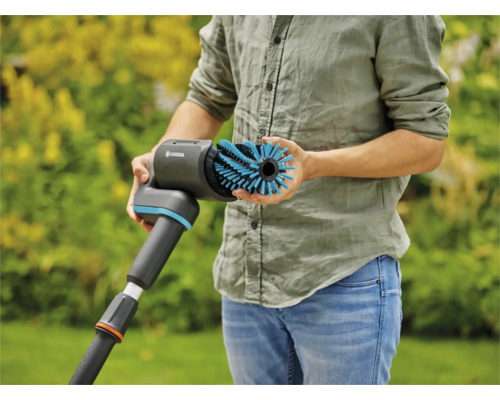 Een persoon houdt een Gardena borstel vast voor het reinigen van oppervlakken buitenshuis