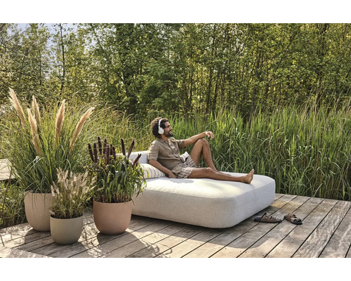 Scène met een man die ontspant op een loungesofa in een tuin met plantenbakken