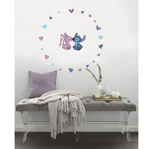 Wanddecoratie met Stitch en Angel, omringd door harten, boven een grijze bank met kussen en deken