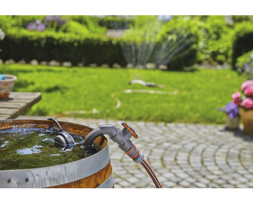 Tuinscene met regenton, kraan en tuinslang voor een groen gazon