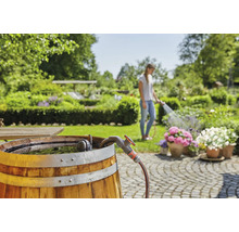 Tuinscene met regenton, kraan en vrouw die bloemen water geeft