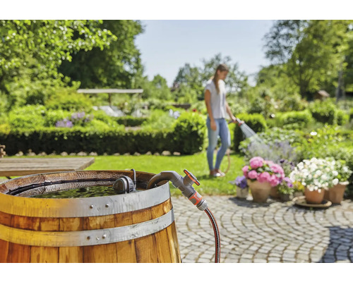 Tuinscene met regenton, kraan en vrouw die bloemen water geeft