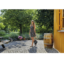 Een vrouw draagt een dompeldrukpomp in een tuin met bomen en bloemen