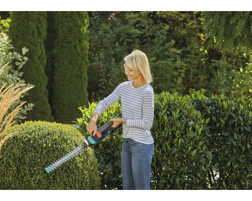 Vrouw snoeit heg met heggenschaar in de tuin.