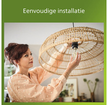 Vrouw installeert een gloeilamp in een hanglamp van rotan