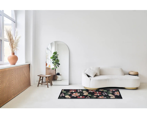 Lichte ruimte met bank, spiegel en deurmat met bloemmotief.