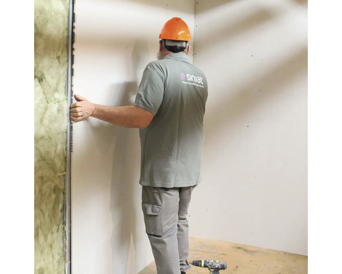 Een vakman installeert een gipsplatenwand met isolatie en metalen frame.