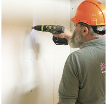 Vakman met beschermhelm boort met een accuschroefboormachine in een muur