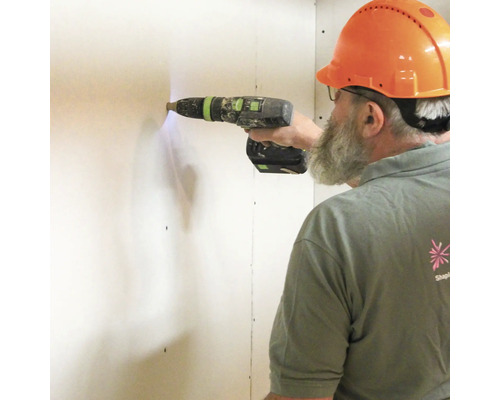 Vakman met beschermhelm boort met een accuschroefboormachine in een muur