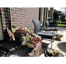 Terras met tuinmeubelen, plantenbakken en decoraties voor een bakstenen muur.
