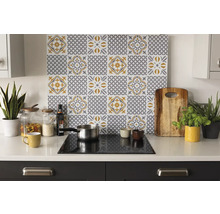 Georganiseerde lichte keuken met een achterwand met grijs-geel tegelpatroon achter een kookplaat op een wit aanrecht met accessoires en planten.