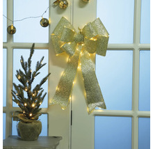 Decoratieve goudkleurige strik met verlichting en kleine spar in juten zak op tafel voor deur