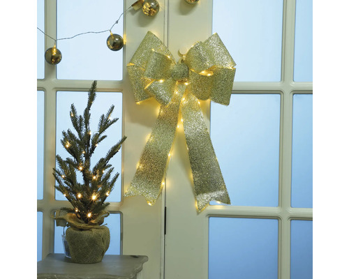 Decoratieve goudkleurige strik met verlichting en kleine spar in juten zak op tafel voor deur