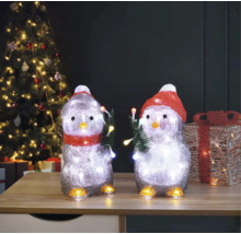 Twee pinguïnfiguren met verlichting en kerstmotief op een tafel voor een kerstboom.