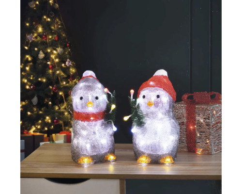 Twee pinguïnfiguren met verlichting en kerstmotief op een tafel voor een kerstboom.