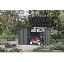 Tuinkast met open deksel en deur in de tuin, met grasmaaier en tuingereedschap