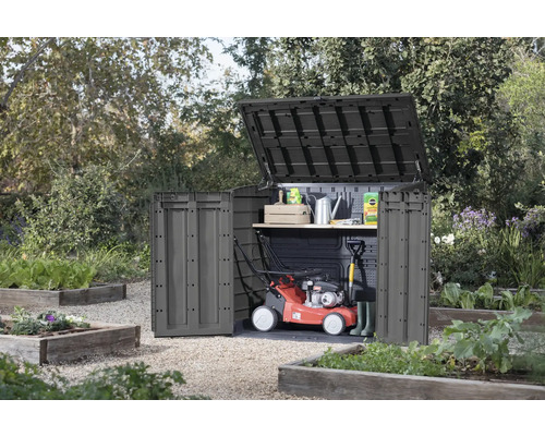 Tuinkast met open deksel en deur in de tuin, met grasmaaier en tuingereedschap