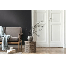 Woonkamer met bank, bijzettafel van gevlochten mandwerk, vaas met takken en houten vloer