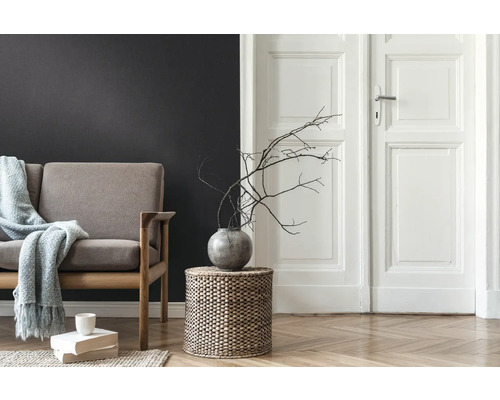 Woonkamer met bank, bijzettafel van gevlochten mandwerk, vaas met takken en houten vloer