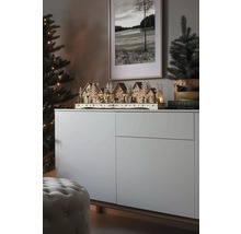 Kerstscène met een verlicht houten dorp op een dressoir, naast een kerstboom en een ingelijste foto.