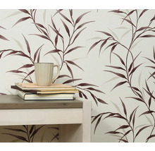 Close-up van een muur met een behang met bladerenmotief, een tafel, boeken en een kop.