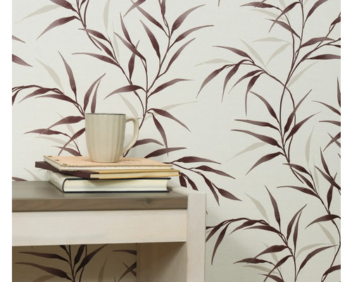 Close-up van een muur met een behang met bladerenmotief, een tafel, boeken en een kop.