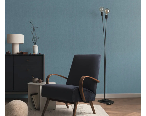 Woonkamer met fauteuil, staande lamp en ladekast voor een blauwe muur
