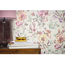 Close-up van een wand met bloemenbehang, aangevuld met een lamp, boeken en een schaal op een houten meubelstuk.